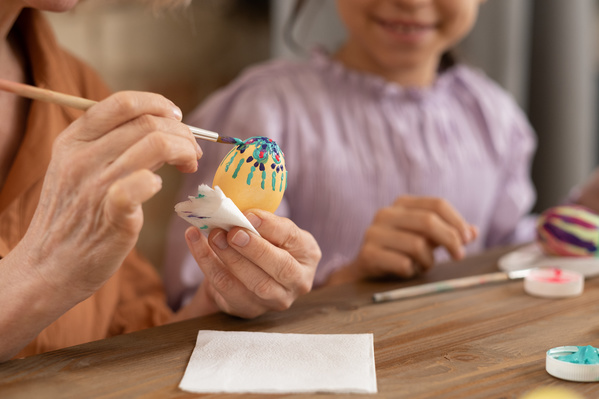 A chicken Easter egg is decorated with a flower design held in the hand with a brush in turquoise paint