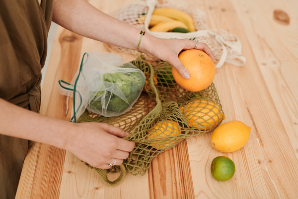 A woman laying out a grapefruit from a string bag filled with vegetables and fruits on a wooden table