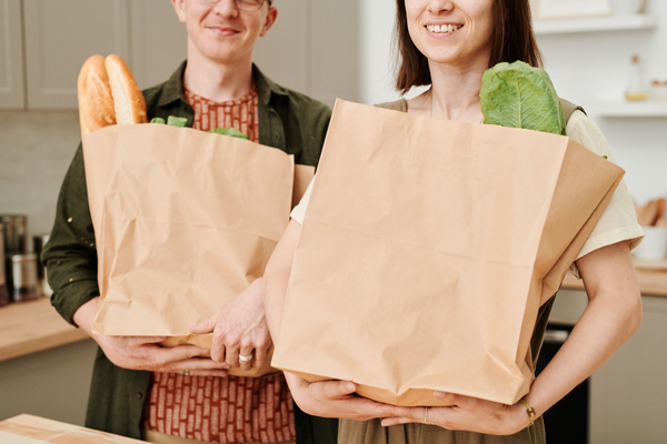 A married couple with grocery shopping in paper bags standing in a bright kitchen