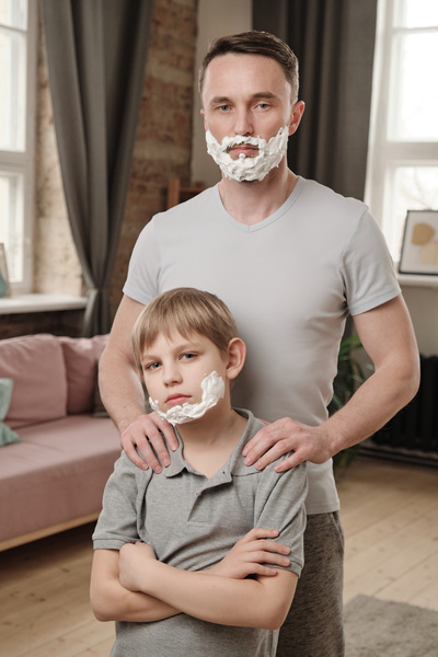 A brutal man and his blond son crossing his arms on his chest both have shaving foam on their chins