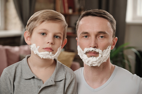 A blond-haired boy and his dad dressed in gray T-shirts with shaving foam on their sad faces