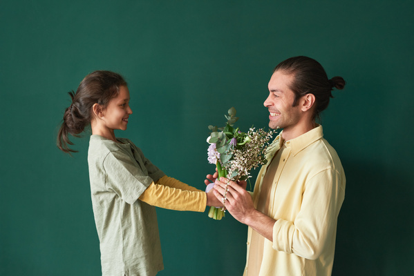 A smiling girl with tidied up hair gives a bouquet of flowers to her father in a yellow shirt