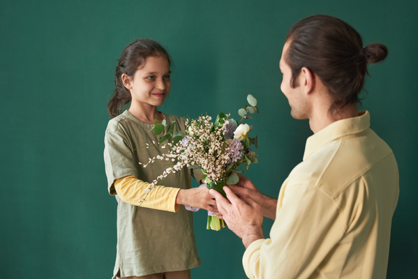 A girl with tidied up hair and her father in a yellow shirt with a bouquet of flowers in their hands