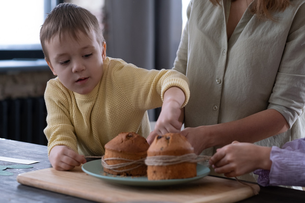 A boy in a yellow sweater and his mother tie a string around Easter pastries on a plate which is on a wooden cutting board