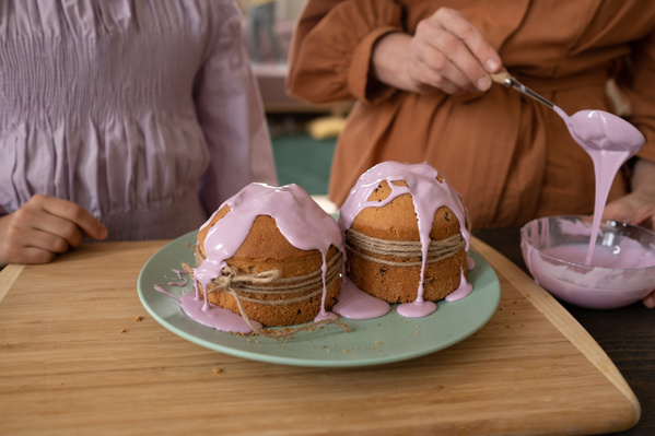 A grandma and granddaughter pouring Easter cakes with pink glaze from a glass bowl