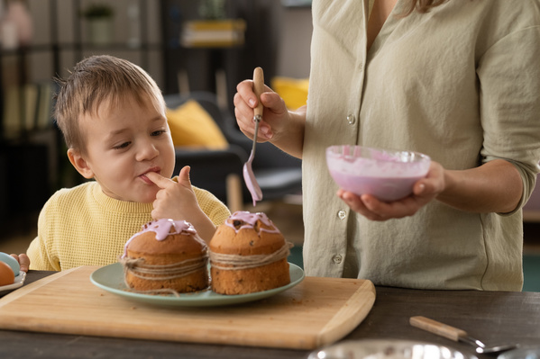 A boy in a yellow sweater tries the pink icing with which his mother covers the Easter cake