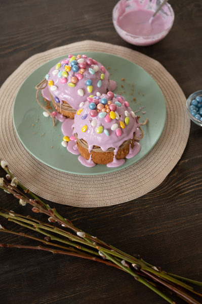 Glazed with pink icing Easter cakes decorated with colored sweets are on a green plate on the table with willow branches