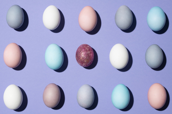 Top view of a shining Easter egg in the middle of other multicolored eggs laid out in rows on a purple background