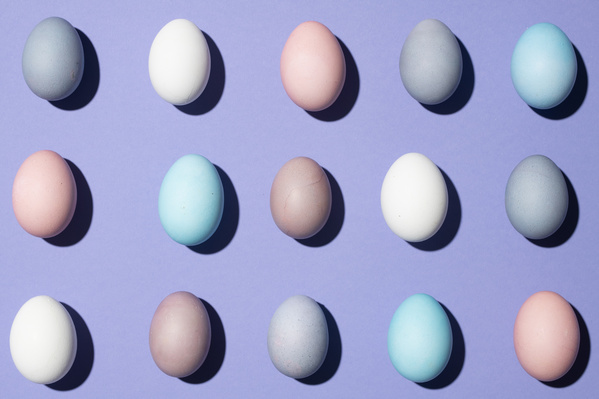 Top view of Easter eggs of different colors laid out in rows on a purple background