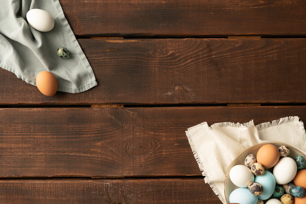 Top view chicken and quail Easter eggs on white and blue cloth napkins on a dark wood table