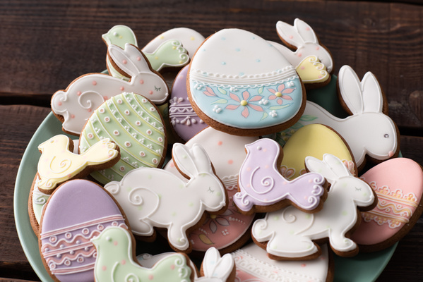 Close-up of a light plate full of beautiful glazed Easter gingerbread with patterns being on a dark wood table