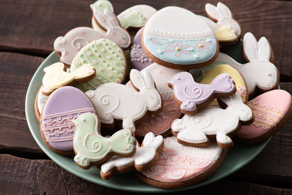 A light-colored plate of glazed Easter cakes of various shapes with patterns standing on a dark wood surface