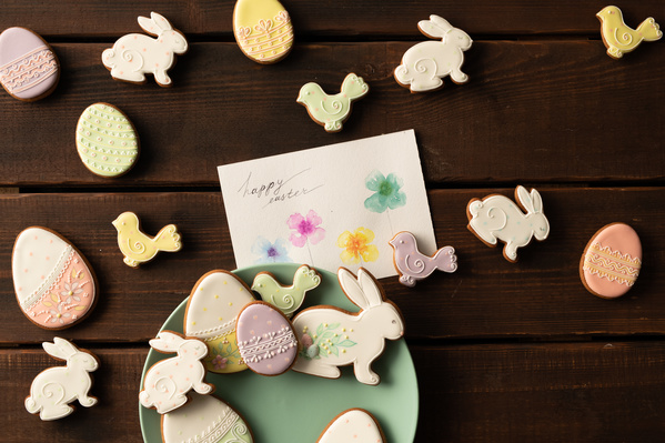 Easter greeting card and glazed gingerbread of different shapes in a thematic style on a plate of green color and on the table of dark wood