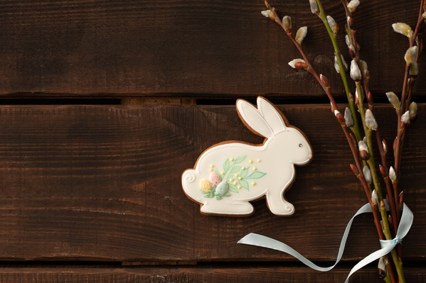 Easter gingerbread in white glaze in the shape of a rabbit with a thematic pattern and a bouquet of willow twigs tied with a blue ribbon