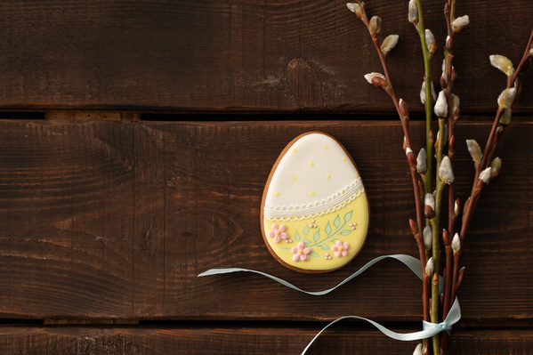 Easter gingerbread in yellow glaze in the shape of an egg with a thematic pattern and a bouquet of willow twigs tied with a blue ribbon