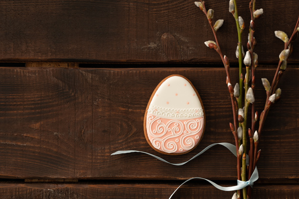 Easter egg-shaped gingerbread in pink icing with a thematic pattern and a bouquet of willow twigs tied with a blue ribbon