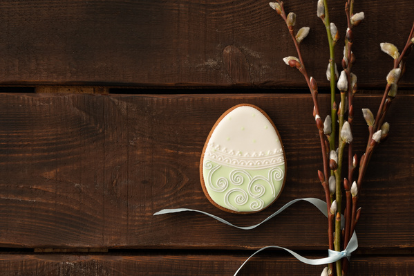 Easter treat in white and green coloring in the shape of an egg with a thematic pattern and willow twigs tied with a blue ribbon
