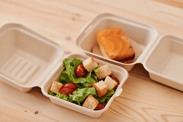 Eco friendly containers for food with caesar salad and fruit pie on a light wood table