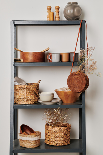 A gray shelving filled with eco-friendly kitchen accessories in straw baskets and glassware of light shades
