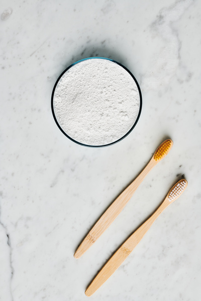 Flatlay of eco toothbrushes and natural tooth powder in a petri dish lying on a marble surface