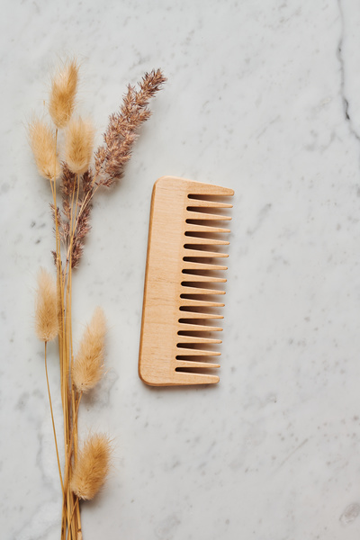 Wooden hair comb with dried flowers lying on a white marble surface