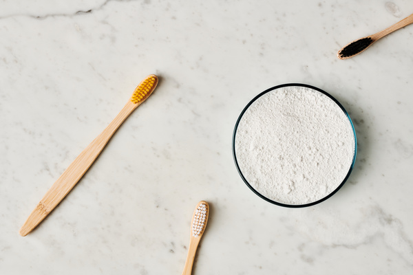 Flatlay of natural toothbrushes and tooth powder in a Petri dish on a marble surface