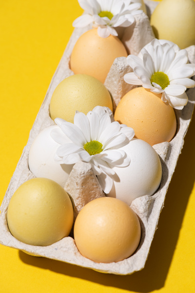 Carton on a yellow surface with hen Easter eggs adorned with white flowers