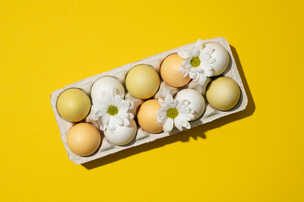 Top view of carton on a yellow background filled with chicken Easter eggs decorated with white daisies