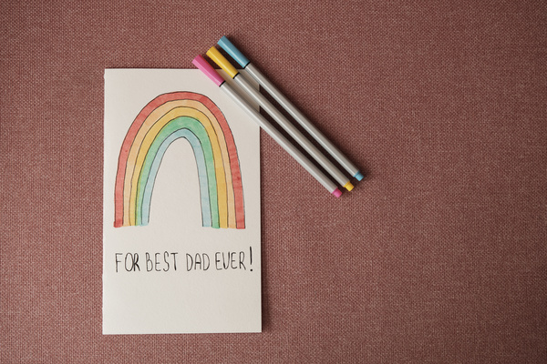 A homemade Fathers Day card with a rainbow image and felt-tip pens on a pink surface