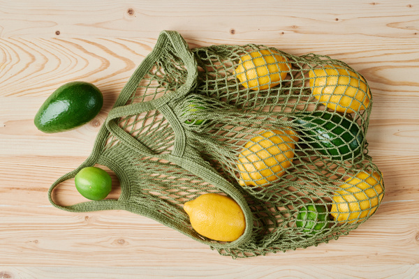 Citrus fruits and avocados lying on a wooden table in a green cotton string bag