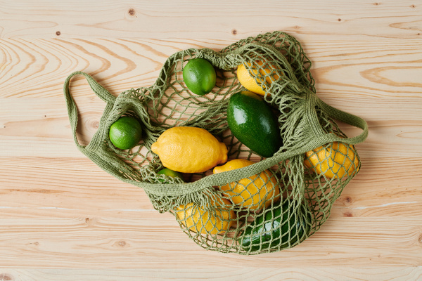 Citrus fruits such as lime and lemon lying in a green cotton bag with avocado