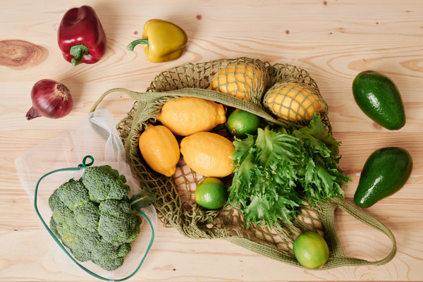 Vegetable and fruit purchases placed in eco-friendly grocery bags on a wooden table