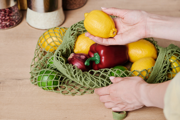 Lemon in a female hand taken from a green cotton string bag with grocery purchases lying on the table