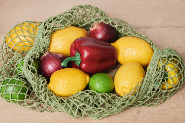 Fresh vegetable purchases in a dark green cotton string bag on a wooden surface