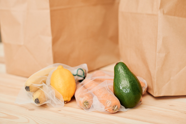 Vegetables and fruits in eco-friendly food bags and avocado with lemon on the kitchen table with paper bags