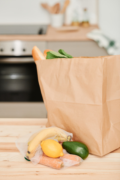 Vegetables laid out in eco-friendly grocery bags and a paper bag with purchases on the kitchen table