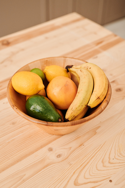 A bamboo bowl full of different fruits is on a wooden kitchen table