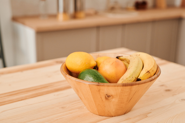 A bamboo bowl filled with various fruits standing on a wooden kitchen table