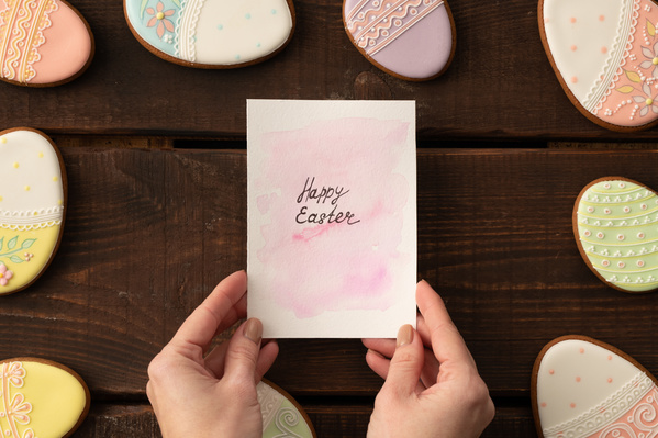 Easter gingerbread in the shape of an egg around a greeting postcard in women's hands