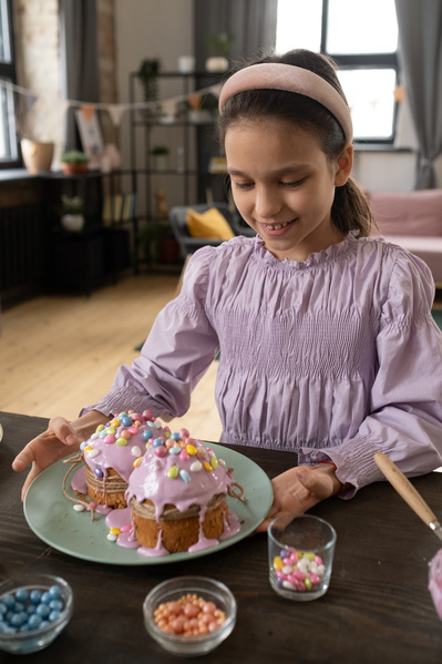 A girl in a pink blouse and with a headband on her head touches a turquoise plate with Easter cakes painted with colorful sweets on the table with confectionery decorations