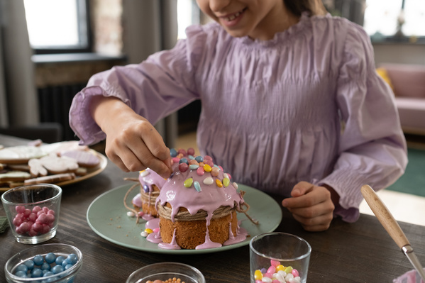 A girl in a pink blouse decorates Easter glazed cakes on a green plate with colorful sweets