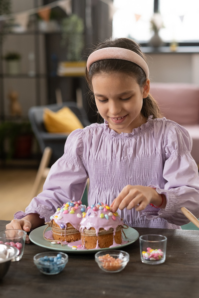 A girl in a pink blouse adorning Easter glazed cakes on a green plate with colored sweets