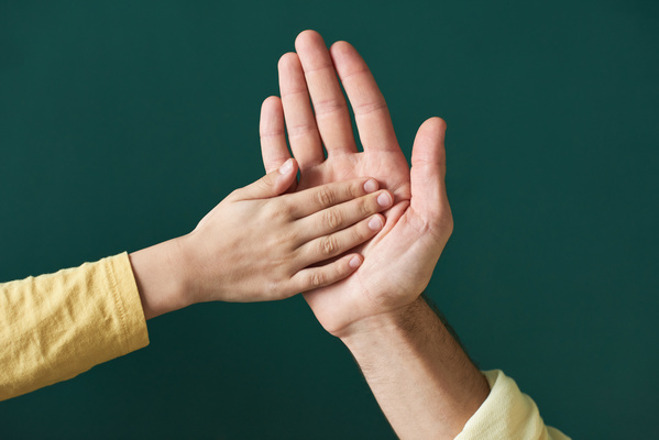 Close-up of the hand of an adult man high-fiving a childs one in a yellow T-shirt with long sleeves