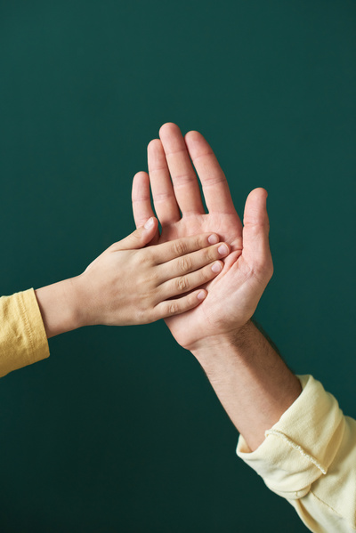 Close-up of the hand of a child in a yellow T-shirt with long sleeves high-fiving an adult one