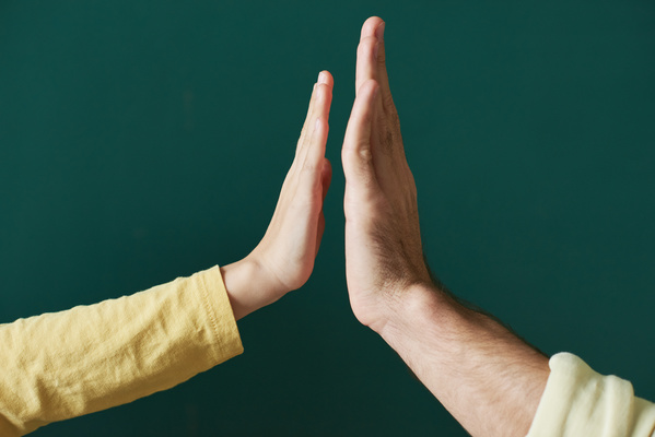 The hand of a child in a yellow longsleeve reaches out to the hand of an adult man against an emerald background