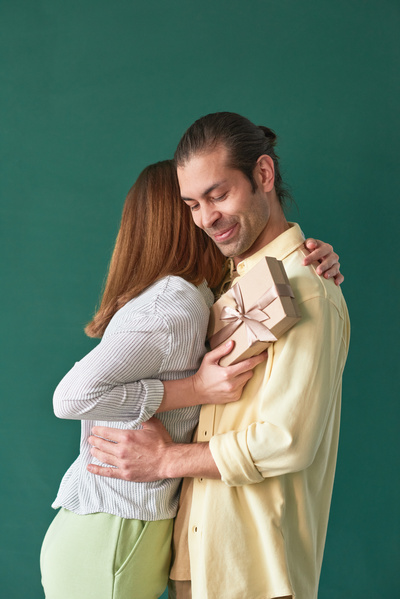 A close-up of a handmade Fathers day card in the hands of a woman who is hugged by her husband