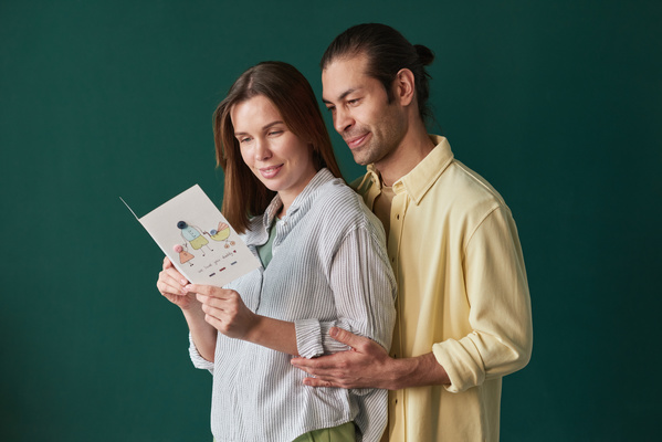 A man in a yellow shirt gently embracing his wife in a striped shirt on an emerald-colored background