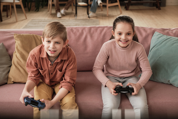 Children sitting on a pink sofa in the living room and excited playing video games with dark gamepads