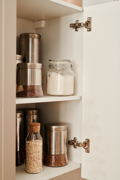 Containers for bulk products filled with grains and flour standing on the shelves of a light kitchen cabinet