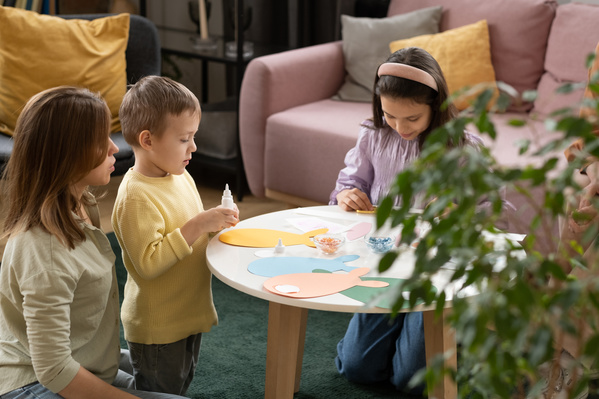 Children and their mother at the white round table making Easter cards in the form of rabbits of different colors